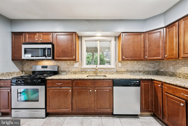 kitchen featuring light stone counters, light tile patterned flooring, a sink, appliances with stainless steel finishes, and decorative backsplash