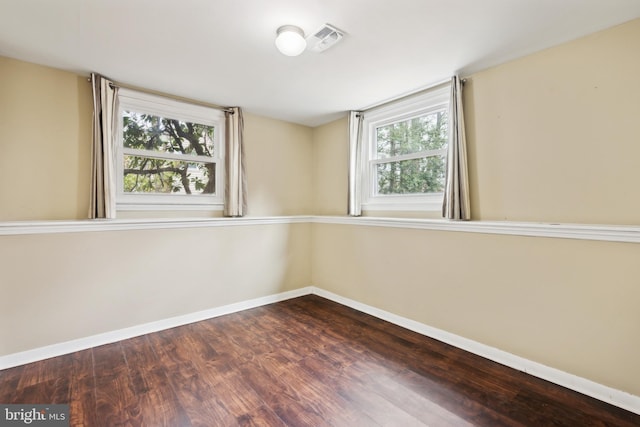 unfurnished room with baseboards, dark wood-style flooring, visible vents, and a healthy amount of sunlight