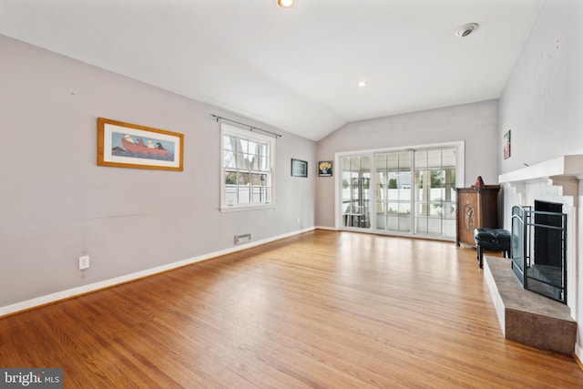 unfurnished living room featuring a fireplace with raised hearth, baseboards, lofted ceiling, and light wood-style floors