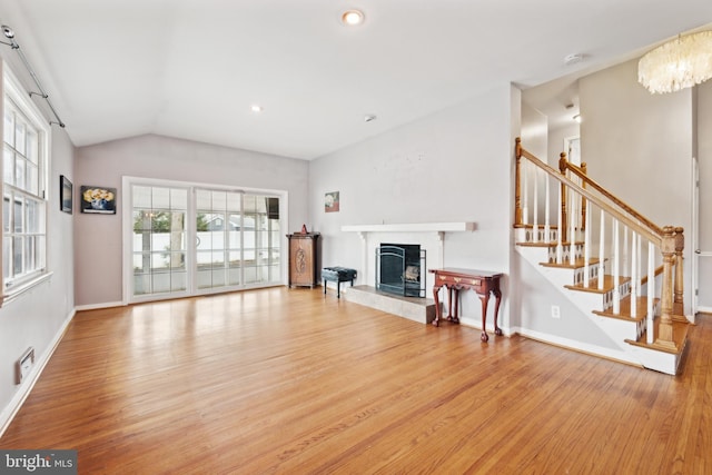 unfurnished living room with lofted ceiling, a premium fireplace, baseboards, stairs, and light wood finished floors