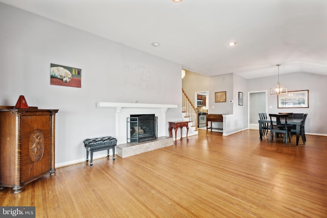 living room featuring a fireplace with raised hearth, vaulted ceiling, light wood-type flooring, and baseboards