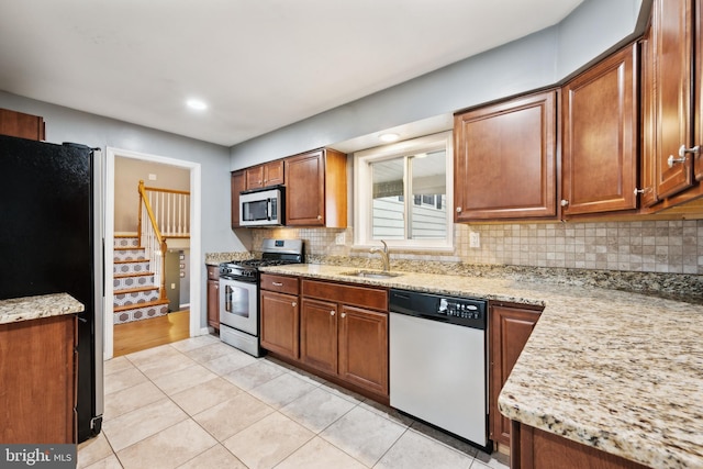 kitchen with light tile patterned floors, a sink, appliances with stainless steel finishes, decorative backsplash, and brown cabinets