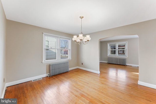 spare room featuring a notable chandelier, light wood-style flooring, radiator, and baseboards