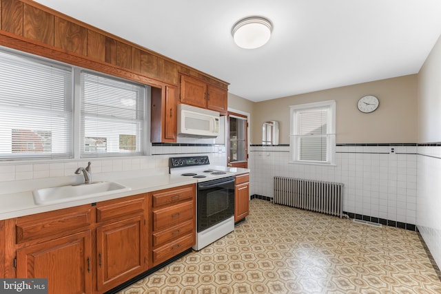 kitchen with a sink, white appliances, radiator, brown cabinetry, and light countertops