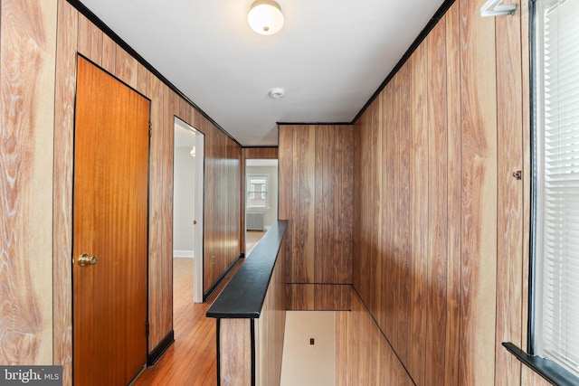 corridor with wooden walls, visible vents, crown molding, an upstairs landing, and light wood-type flooring