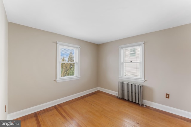 unfurnished room featuring radiator heating unit, a healthy amount of sunlight, baseboards, and light wood finished floors