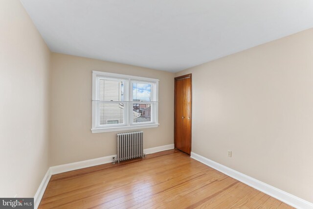 empty room with baseboards, radiator heating unit, and light wood-style floors