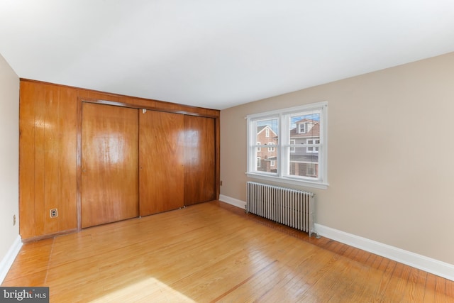 unfurnished bedroom with a closet, light wood-type flooring, radiator heating unit, and baseboards