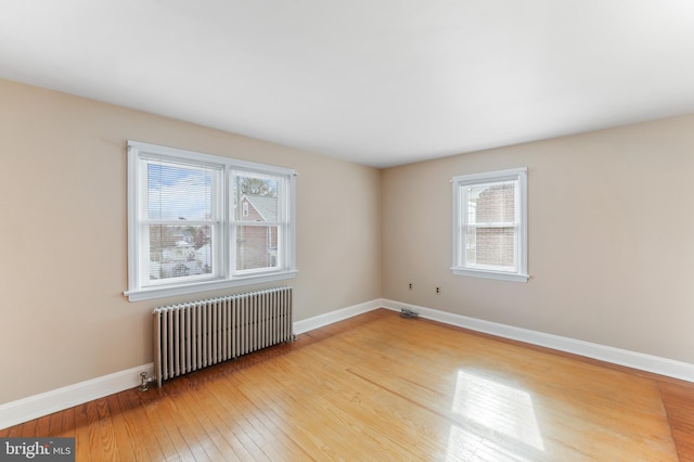 unfurnished room featuring radiator heating unit, baseboards, and wood-type flooring