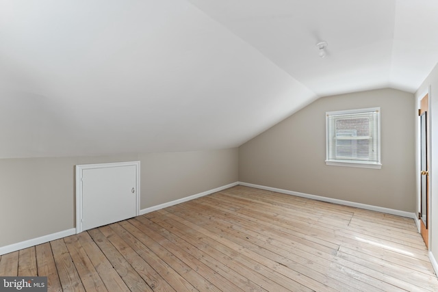 bonus room with baseboards, light wood-style floors, and lofted ceiling