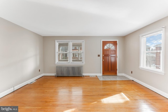 foyer entrance with visible vents, baseboards, light wood-style flooring, and radiator heating unit