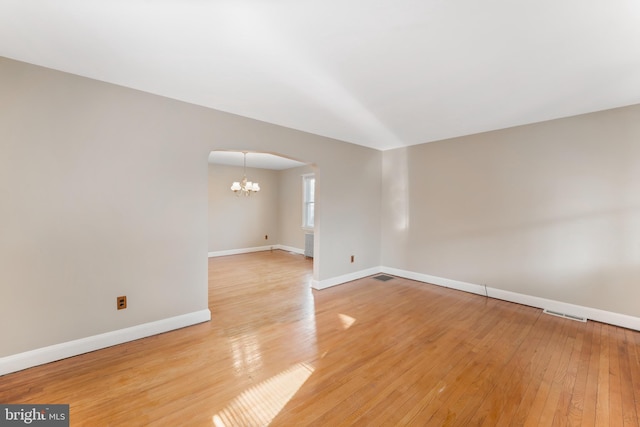 spare room with visible vents, baseboards, light wood-style flooring, arched walkways, and a notable chandelier