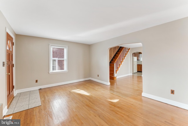 spare room featuring stairway, arched walkways, baseboards, and light wood-style flooring