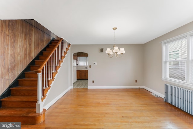 interior space featuring radiator heating unit, arched walkways, light wood-style floors, baseboards, and stairs