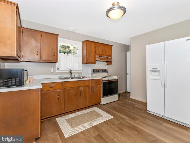 kitchen with under cabinet range hood, white appliances, a sink, light countertops, and brown cabinetry