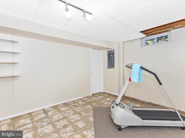 exercise area featuring baseboards, electric panel, tile patterned floors, concrete block wall, and track lighting