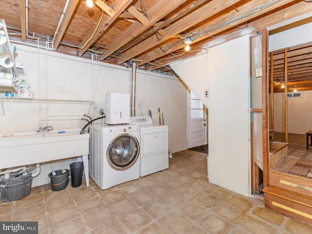 laundry area featuring concrete block wall, laundry area, washing machine and dryer, and a sink