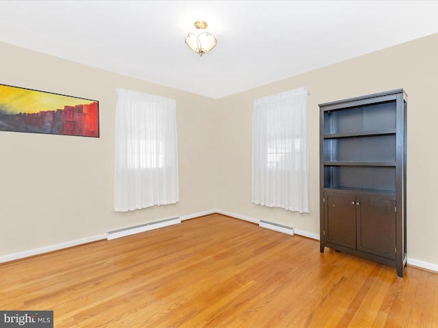 spare room featuring a baseboard radiator, a healthy amount of sunlight, light wood-style flooring, and baseboards