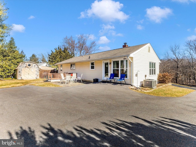 view of front of property with a chimney, an outbuilding, a deck, central air condition unit, and a shed