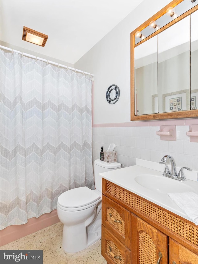 full bathroom with toilet, a wainscoted wall, speckled floor, vanity, and tile walls