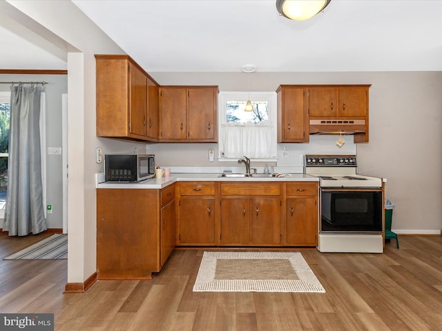 kitchen with white range with electric cooktop, light countertops, stainless steel microwave, a sink, and under cabinet range hood