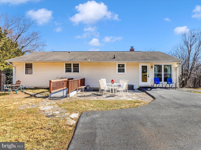 back of house featuring a patio, a chimney, and a lawn