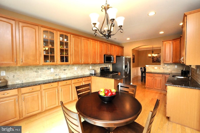 kitchen featuring arched walkways, appliances with stainless steel finishes, glass insert cabinets, a sink, and a chandelier