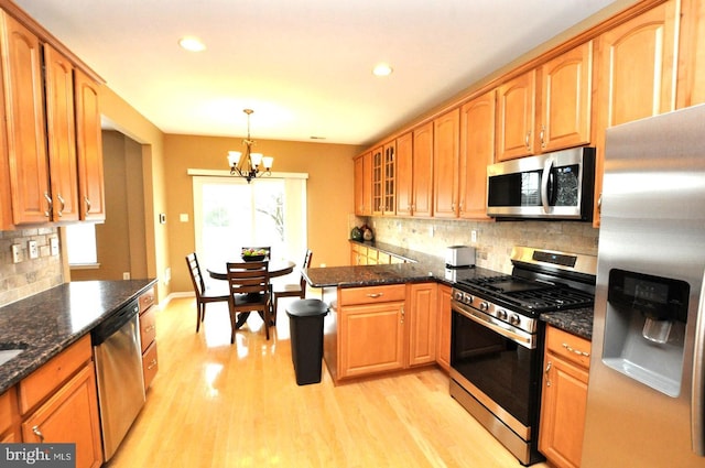 kitchen with glass insert cabinets, a peninsula, stainless steel appliances, light wood-type flooring, and a chandelier