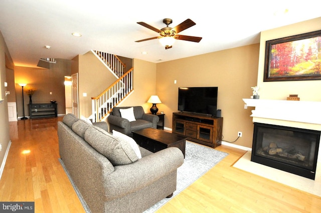 living area featuring recessed lighting, stairway, a glass covered fireplace, wood finished floors, and baseboards