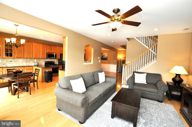 living room featuring light wood-style flooring, recessed lighting, stairway, and ceiling fan with notable chandelier