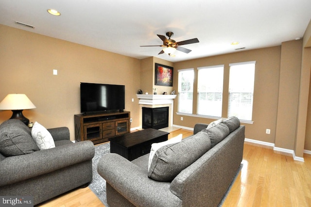 living area with visible vents, light wood-style floors, a fireplace with flush hearth, a ceiling fan, and baseboards