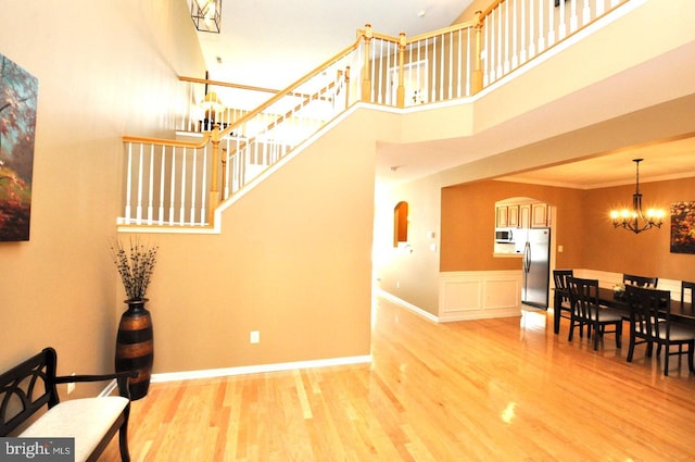 stairway featuring baseboards, a towering ceiling, wood finished floors, crown molding, and a notable chandelier