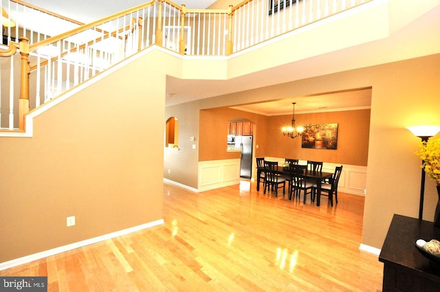 dining room with arched walkways, light wood-style flooring, a towering ceiling, ornamental molding, and an inviting chandelier