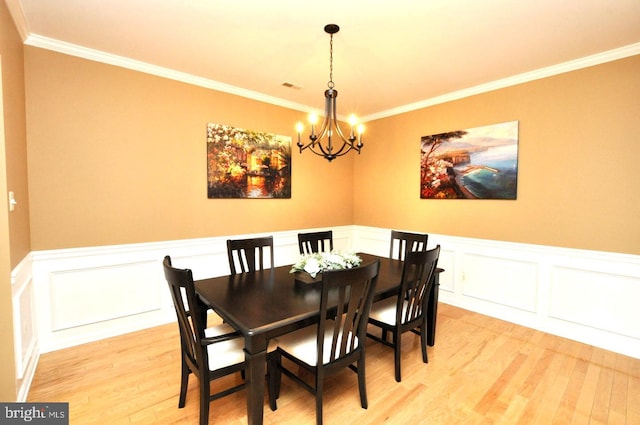 dining space with crown molding, a notable chandelier, visible vents, light wood-style flooring, and wainscoting