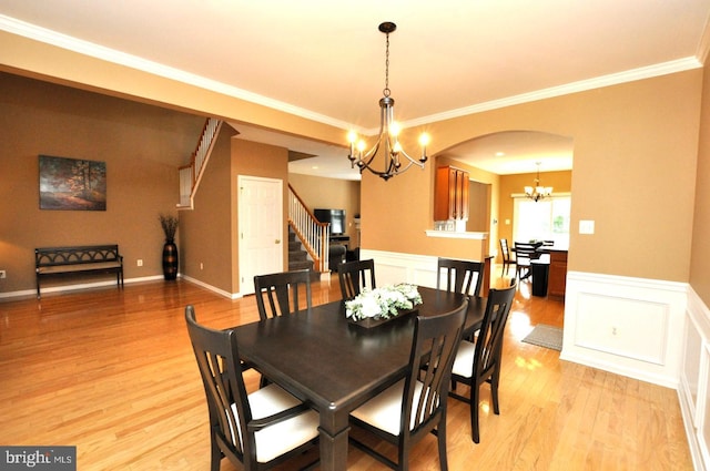 dining room with an inviting chandelier, ornamental molding, wainscoting, light wood-type flooring, and stairs