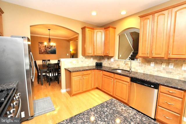 kitchen featuring decorative backsplash, appliances with stainless steel finishes, a sink, light wood-style floors, and a notable chandelier