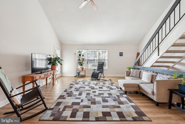 living room with vaulted ceiling, a textured ceiling, wood finished floors, baseboards, and stairs