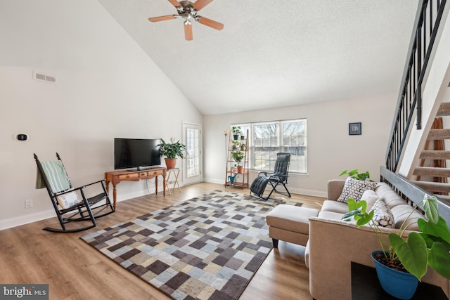 living area with high vaulted ceiling, wood finished floors, visible vents, baseboards, and stairway