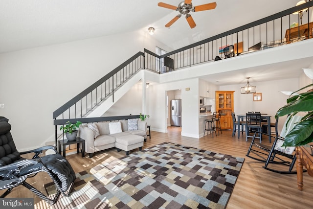 living area with baseboards, wood finished floors, stairs, a high ceiling, and ceiling fan with notable chandelier