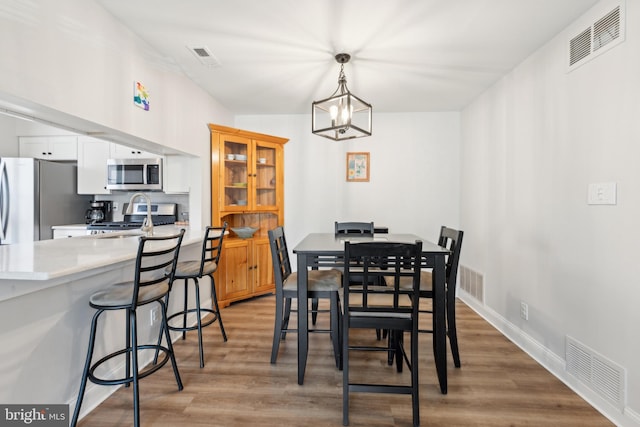 dining area featuring an inviting chandelier, light wood-type flooring, visible vents, and baseboards