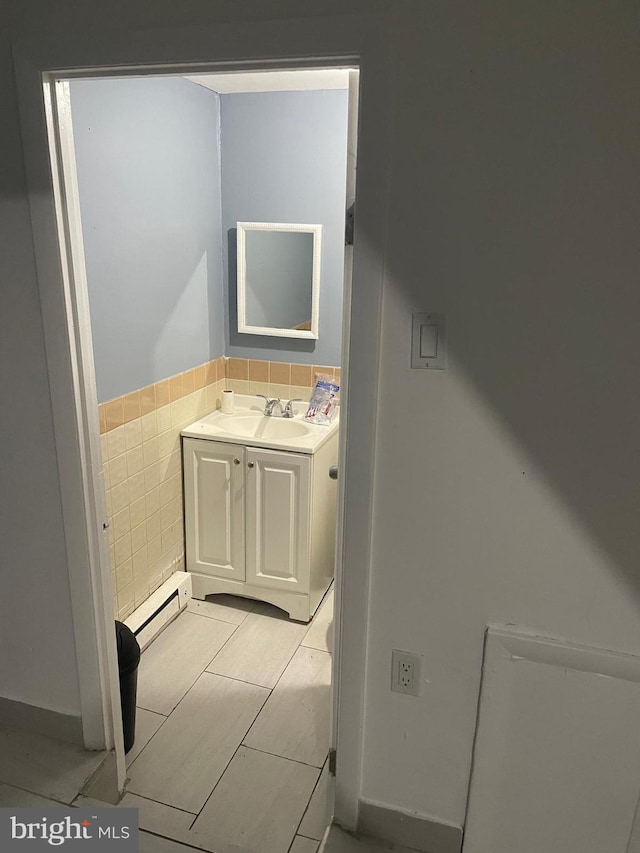 bathroom featuring a wainscoted wall, a baseboard heating unit, tile walls, and vanity