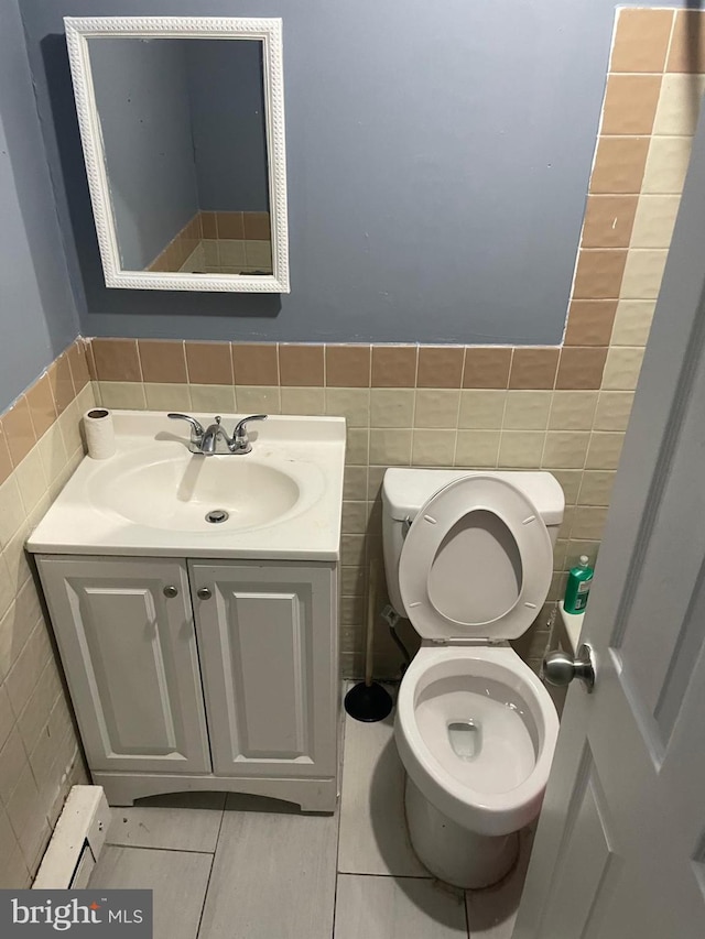 half bathroom featuring toilet, wainscoting, vanity, and tile walls