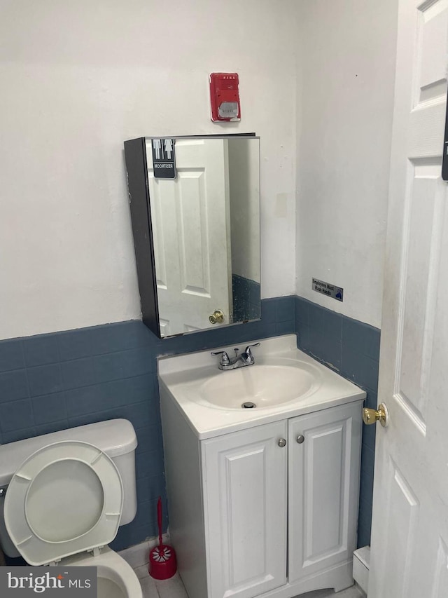 bathroom with toilet, a wainscoted wall, tile walls, and vanity