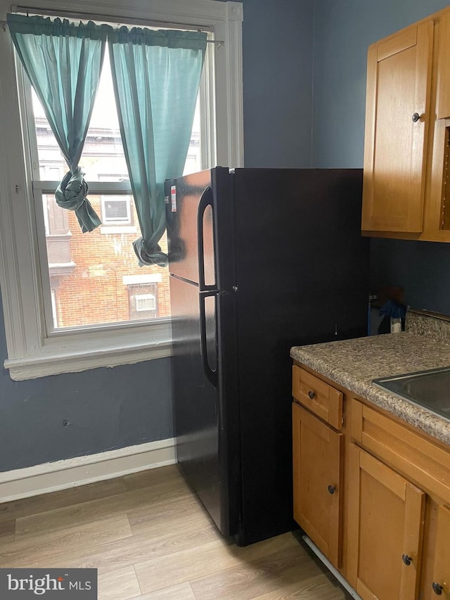 kitchen with light wood finished floors, a sink, freestanding refrigerator, and baseboards