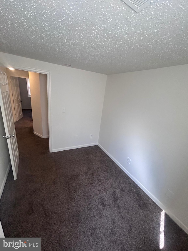 spare room featuring a textured ceiling, carpet, and baseboards