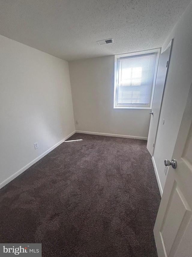 unfurnished bedroom with visible vents, baseboards, a textured ceiling, and dark carpet