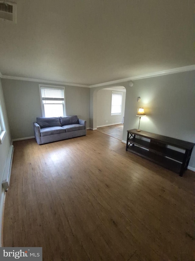 unfurnished living room featuring crown molding, wood finished floors, baseboard heating, baseboards, and arched walkways