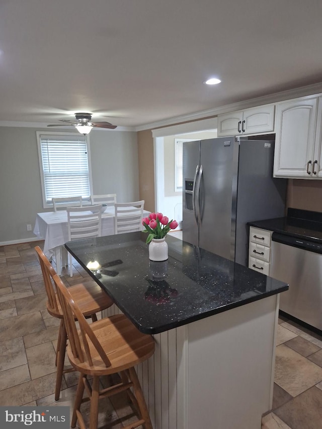 kitchen featuring stone finish flooring, a kitchen bar, stainless steel appliances, dark stone counters, and white cabinetry