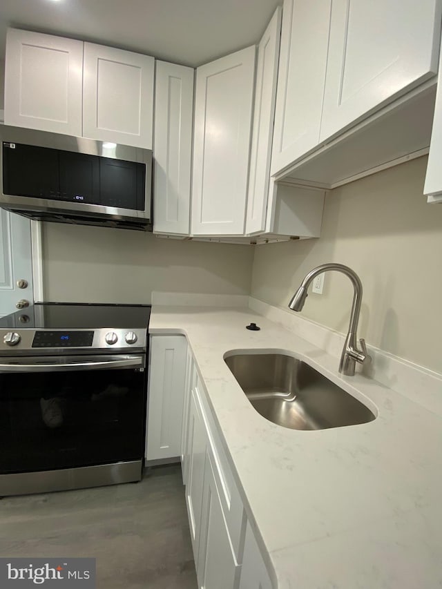 kitchen with a sink, stainless steel appliances, light stone countertops, and white cabinetry