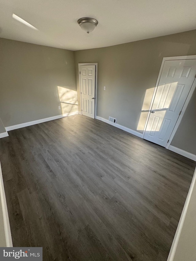 unfurnished room with visible vents, baseboards, and dark wood-type flooring